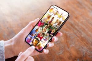 Osoba trzyma w obu dłoniach czarnego smartfona i robi za jego pomocą zdjęcie swojej c&oacute;rce, kt&oacute;ra puszcza bańki mydlane