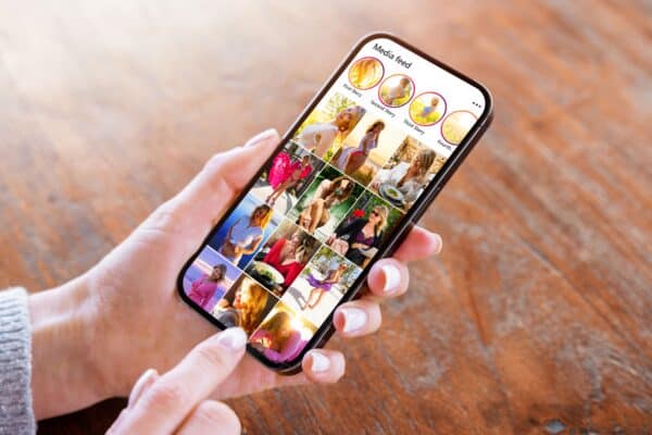 Jak przechowywać zdjęcia na urządzeniu - poradnik Osoba trzyma w obu dłoniach czarnego smartfona i robi za jego pomocą zdjęcie swojej córce, która puszcza bańki mydlane